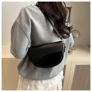 Detail of matte black saddle bag with vintage flap and gold metal buckle on shoulder