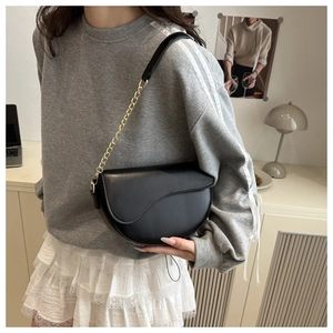 Close-up of a black leather saddle bag with gold chain strap on a stylish model