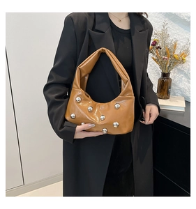 Detail of caramel glossy leather handbag with silver stud accents on a model