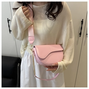 Pink saddle bag with wide fabric strap and gold chain shown on a female model