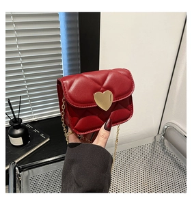Close-up of red quilted crossbody bag featuring a golden heart-shaped lock and chain strap