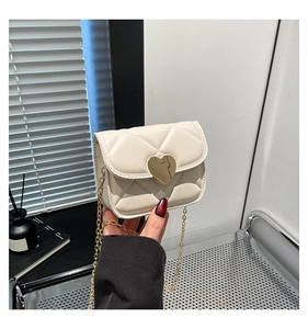 Detail of cream quilted mini bag featuring a gold heart clasp and fine chain strap