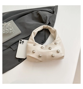 Detail of a beige half-moon hobo bag with metallic rivet accents on a minimal background