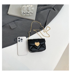 Flat lay of mini black quilted bag with gold heart clasp next to a smartphone