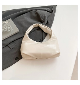Close-up of cream leather shoulder bag featuring unique pleated texture and rivet details