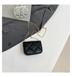 Top view of black quilted mini bag with gold chain strap on a grey blazer backdrop