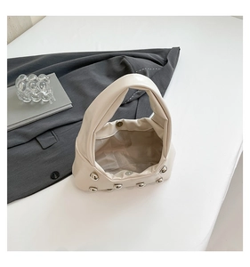 Detail view of cream handbag with silver studs and magnetic closure on white surface