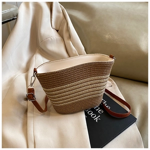 Dettaglio della borsa a secchiello in paglia intrecciata con tracolla in pelle su blazer bianco