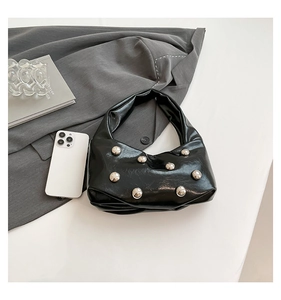 Detail of glossy black leather handbag featuring large silver stud rivets and a sleek handle