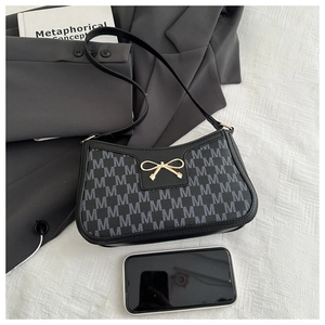 Dettaglio borsa baguette nera con chiusura a fiocco dorato e monogramma M