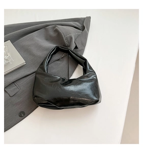 Detail of black crinkled patent leather underarm bag on a stylish blazer background