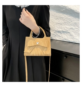 Detail of yellow bow handbag featuring heart-shaped crystal on premium leather