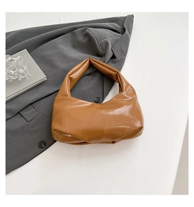 Detail of caramel glossy underarm bag featuring a unique gathered pleated handle design