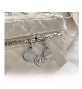 Detail view of cream quilted bag featuring dual zippers and a silver camellia charm