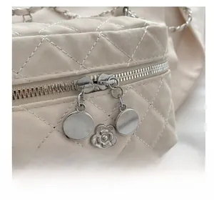 Detail of silver dual zippers and camellia flower charm on cream quilted bucket bag