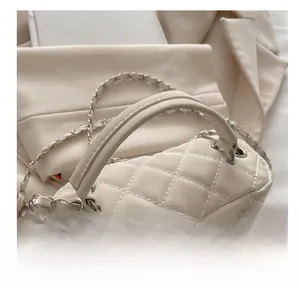 Detailed macro of cream quilted chain bag featuring elegant metal pendants and dual zippers