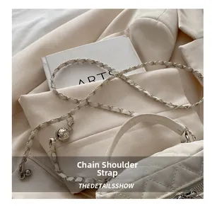 Detail of white quilted handbag featuring leather-woven chain and gold adjustment ball