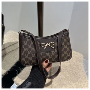 Dettaglio borsa baguette marrone con fibbia a fiocco dorato e motivo monogramma M