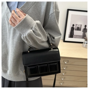 Detail of black leather handbag with embossed pattern and gold hardware in cozy indoor setting