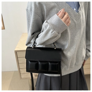 Detail of black crossbody bag featuring chocolate block stitching and metallic clasp