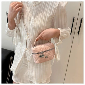 Close-up of pink quilted mini bucket bag with chain strap and flower charm on white outfit