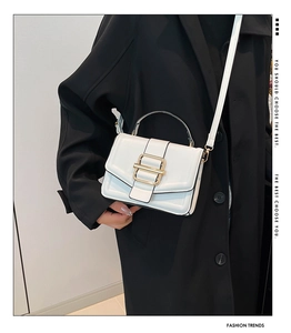 Close-up of white crossbody bag with gold buckle on black coat background