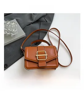 Close-up of brown leather crossbody bag with elegant gold buckle on a stylish suit
