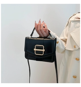 Detail of minimalist black handbag featuring a bold gold buckle and slender strap