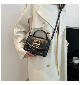 Detail of a chic black leather crossbody bag with gold buckle worn with a beige trench coat