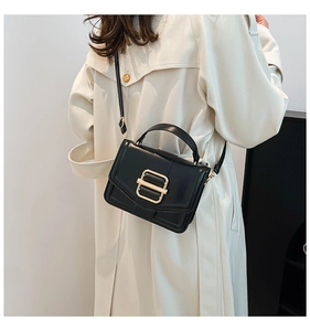 Classic black leather crossbody bag with large gold buckle styled on a beige trench coat