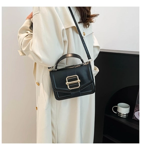 Detail of minimalist black crossbody bag with shiny gold buckle on cream trench coat