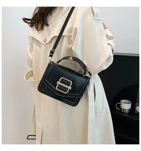 Detail of minimalist black crossbody bag with bold gold square buckle on trench coat