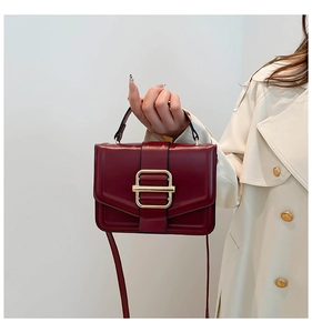 Detail of dark red square crossbody bag with gold metallic buckle and leather texture