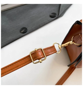Close-up of adjustable golden buckle and lobster clasp on brown leather crossbody bag