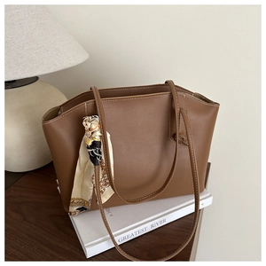 Brown leather tote bag detail with decorative printed scarf on a wooden table with book