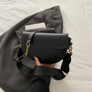 Classic black saddle bag with gold chain and wide strap in a minimalist urban setting