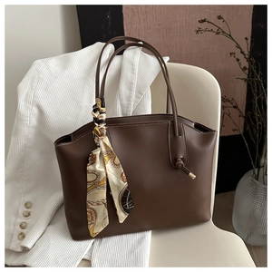 Detail of dark brown leather tote bag with white stitching and floral silk scarf charm