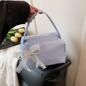 Close-up of light blue handbag with lace bow pearl charm held in hand against flowers