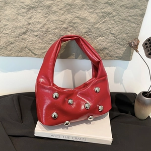 Red patent leather underarm bag with silver studs on a stylish stone background