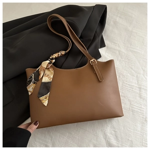 Detailed view of brown leather tote bag with decorative silk scarf and metal hardware