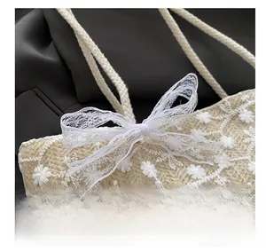 Détail de la broderie en dentelle florale blanche et d'un nœud sur un sac en paille