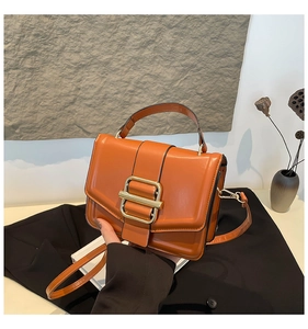 Detail of bright orange handbag featuring a golden square buckle and smooth texture