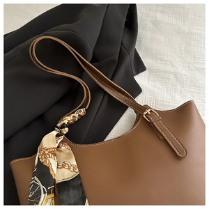 Detail of a brown leather tote bag with contrast stitching and decorative silk scarf accessory