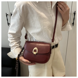 Close-up of wine red saddle bag with gold horseshoe buckle and woven tassel detail