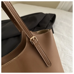 Close-up of brown leather tote bag with white stitching and adjustable gold metal buckle