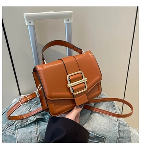 Close-up of caramel faux leather bag with gold rectangular buckle on denim jacket