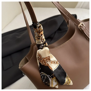 Detailed close-up of brown leather tote texture with silk scarf on the handle