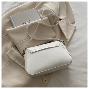 Detail of white leather shoulder bag with a sleek flap design on an ivory blazer