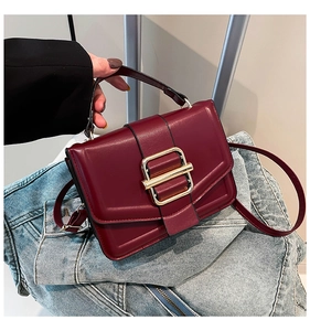 Detail of burgundy leather handbag with gold metallic buckle and precise stitching