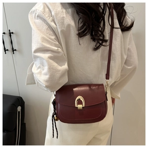 Detail of burgundy saddle bag featuring gold horseshoe buckle worn by model